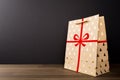 Christmas Brown Paper Bag with Red Ribbon and glittering golden trees on wooden table isolated on black background, glittering Royalty Free Stock Photo