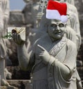 Christmas buddhist monk statue pointing at a gift that says present moment and wearing a santa claus hat Royalty Free Stock Photo