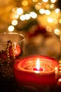 Christmas candle close-up view with glowing flame and ornaments and a crystal jar with blurred tree lights as background Royalty Free Stock Photo
