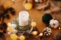 Christmas candle in rustic holder made of branches, cotton, anise and pine cones on wooden table in festive lights bokeh. Making Royalty Free Stock Photo