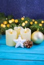 Christmas candles with fire, white sparkling star, golden pine cone and ball on blue wooden background. Behind there are spruce Royalty Free Stock Photo