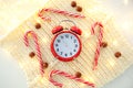 Christmas candy cane, garland and red alarm clock on white knitted background, copy space. Winter minimalistic flat lay. Still lif