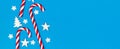 Christmas candy cane lied evenly in row on blue background with decorative snowflake and star. Flat lay and top view