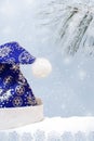 Blue decorated with snowflakes hat Santa Claus on snow on background of snow-covered pine branch and row of snowflakes. Royalty Free Stock Photo