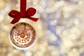 Cup of fragrant hot coffee with white foam and cinnamon snowflake made from Christmas ball, bauble hangs on a red ribbon Royalty Free Stock Photo