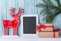 Christmas card with empty chalkboard, deer and gift boxes, wooden background with fir tree branch