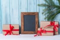 Christmas card with empty chalkboard and gift boxes, wooden background with fir tree branch