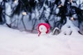 Christmas card with a festive cute toy snowman in a bright pink cap sitting in a snowdrift with a gift under the Christmas tree in Royalty Free Stock Photo