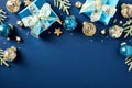 Christmas card. Flat lay glistening blue paper gift boxes, gold and blue Xmas balls ornaments, fir branches, confetti on dark blue Royalty Free Stock Photo