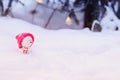 Christmas funny toy snowman in a bright pink cap sitting in a snowdrift with a gift under the tree in the winter Park Royalty Free Stock Photo