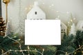 Christmas card mock up. Empty greeting card on background of stylish christmas houses, fir branches with golden lights and tree Royalty Free Stock Photo