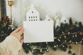 Christmas card mock up. Hand holding empty greeting card on background of stylish christmas houses, fir branches with golden Royalty Free Stock Photo