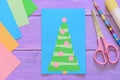 Christmas card, scissors, glue stick, pencil, colored paper on purple wooden background. Creative greeting card Royalty Free Stock Photo