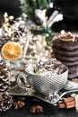 Christmas card silver cup of sweet cream on black table, with sweets, cinnamon, aniseed, winter cone, and empty glass