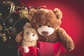 Christmas card with Teddy and banny in red gift bags under the Christmas tree. With holiday decoration and presents
