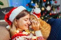 Christmas celebration with cat. Woman playing and hugging pet in Santa`s hat by New year tree at home Royalty Free Stock Photo