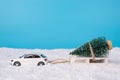 Christmas celebration concept. Close up photo of toy mini car carrying white wooden sledge with little christmas tree on isolated Royalty Free Stock Photo