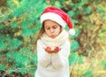 Christmas child little girl in santa red hat blowing snow lying on her hands over tree Royalty Free Stock Photo