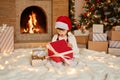 Christmas child opening present near xmas tree. Happy baby girl with New Year gift box sitting on floor with astonished facial Royalty Free Stock Photo