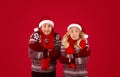 Christmas chill. Young couple in winter outfits shivering on red background Royalty Free Stock Photo