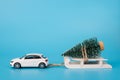 Christmas is coming soon concept. Close up photo of toy mini car carrying little christmas tree on white wooden sledge isolated on Royalty Free Stock Photo