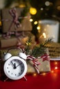 Christmas composition, alarm clock shows five to midnight, gifts on a red background, soft focus treats in the background for