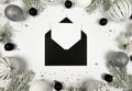 Christmas composition, black envelope, white and silver decorations, fir tree branches, silver stars confetti on white background. Royalty Free Stock Photo