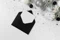 Christmas composition, black envelope, white and silver decorations, fir tree branches, silver stars confetti on white background. Royalty Free Stock Photo