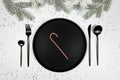 Christmas composition, black plate and cutlery, fir tree branch, candy cane, silver stars confetti on white background. Royalty Free Stock Photo