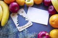 Christmas composition of fruits, white empty leaf in the middle with a wooden blank of a Christmas tree around apples, tangerines Royalty Free Stock Photo