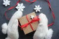 Christmas composition. Gift box with red satin ribbon holding hands in white fur mittens. Royalty Free Stock Photo