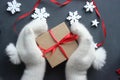 Christmas composition. Gift box with red satin ribbon holding hands in white fur mittens. Royalty Free Stock Photo