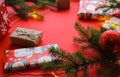 Christmas composition with gift boxes, clews of rope, paper`s rools and decorations, fir tree branches on red background.