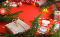 Christmas composition with gift boxes, clews of rope, paper`s rools and decorations, fir tree branches on red background.