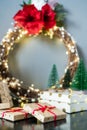 Christmas composition with gift boxes, red lantern, small Christmas trees decor and elegant flower wreath on black table on gray