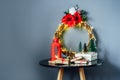 Christmas composition with gift boxes, red lantern, small Christmas trees decor and elegant flower wreath on black table