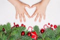 Christmas composition with kid hands making heart, green Xmas fir branch, red holly berries and baubles on white background. Royalty Free Stock Photo