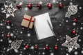 Christmas composition. Paper blank with pen and gift, red and white decorations on black wooden background Royalty Free Stock Photo