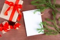 Christmas composition. Three gifts, fir branches and blank notepaper on a dark wooden background. Flat lay, top view. Copy space