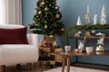 Christmas composition of warm living room interior with christmas tree, balls, gifts, wooden coffee table, white armchair, candle Royalty Free Stock Photo