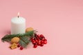 Christmas composition with white candle, spruce twig, walnuts and cranberries on a pink background Royalty Free Stock Photo