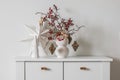 Christmas composition on a white chest of drawers - a Christmas bouquet with cranberry branches and paper decorations, a Christmas