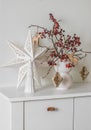 Christmas composition on a white chest of drawers - a Christmas bouquet with cranberry branches and paper decorations, a Christmas