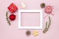 Christmas composition. White photo frame, fir branches, cones, red ball, twine, gift, wooden toys on pink background Flat lay top