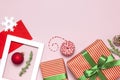 Christmas composition. White photo frame, red envelope, fir branches, cones, ball, twine, gift, wooden toys on pink background