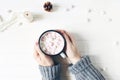 Christmas composition. Woman`s hands in sweater holding cup of hot chocolate. Marshmallows, pine cones and silk ribbon Royalty Free Stock Photo