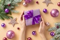 Christmas concept. First person top view photo of female hands holding lilac giftbox with purple bow over pink violet baubles Royalty Free Stock Photo