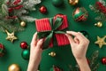 Christmas concept. First person top view photo of woman`s hands untying ribbon bow on red giftbox over gold green baubles star Royalty Free Stock Photo