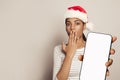 Christmas concept. Nice surprised woman in Santa hat holding smartphone with empty white screen display, Mockup banner Royalty Free Stock Photo