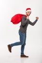 Christmas concept - Young confident beard man running and holding red big santa bag with a lot of present inside. Royalty Free Stock Photo